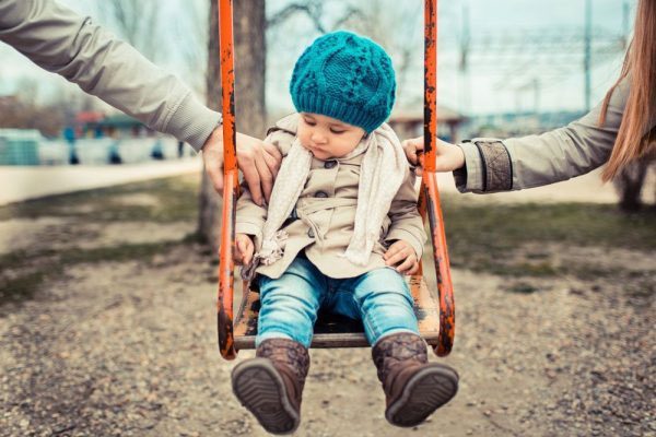 a little girl on a swing being held by two parents